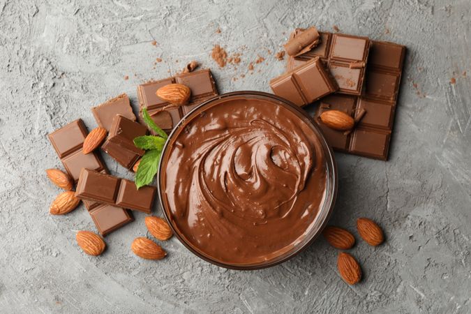 Bowl with chocolate and chocolate pieces on gray background