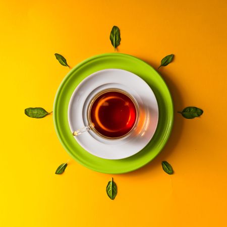 Tea in glass cup with green leaves  on orange background