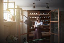 Smiling woman in leather apron holding handmade plates in her shop