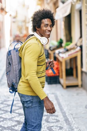 Man in backpack and headphones turning around in pedestrian street
