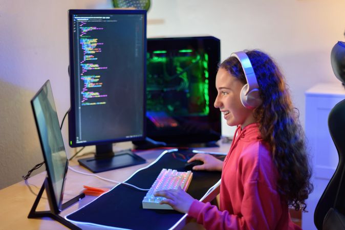Happy teenage girl in headphones sitting at table and playing games in room