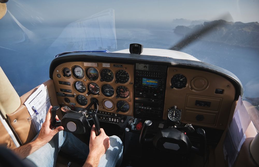 Crop faceless pilot operating biplane above blue sea