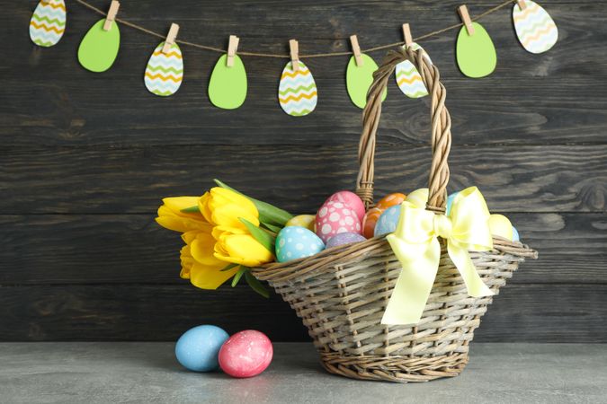 Easter basket filled with colorful eggs and flowers on a wooden background