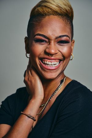 Closeup portrait of smiling Black woman with septum piercing, with hand to her neck