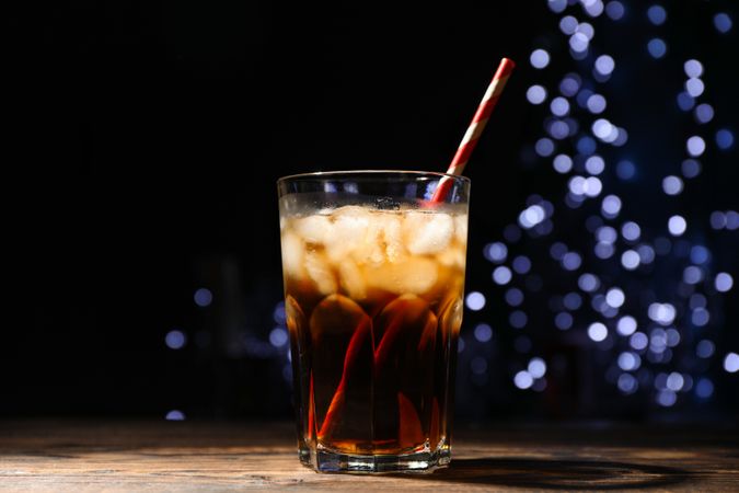 Glass with cola, lime slice and tubule against blurred lights background