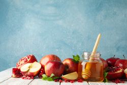 Delicious apple halves, pot of honey with dipper and pomegranates on table