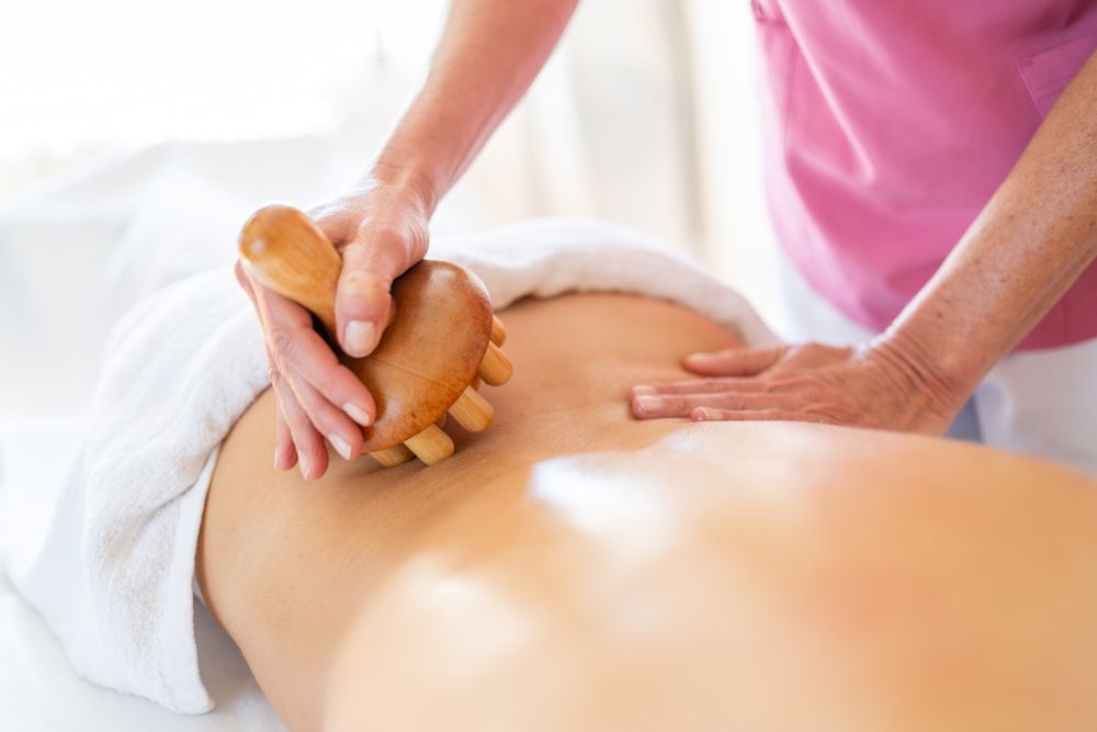 Crop masseur massaging back of client in physiotherapy clinic with wooden therapy tool