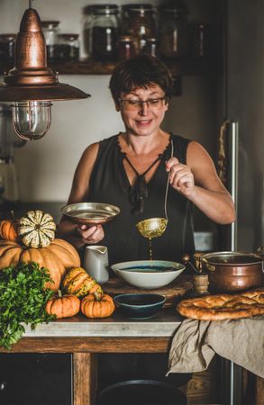 Woman with short hair and glasses with soup ladle in kitchen in cozy kitchen