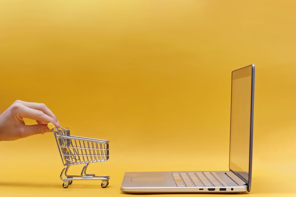 Online Shopping Concept with Mini Cart and Laptop on Yellow Background