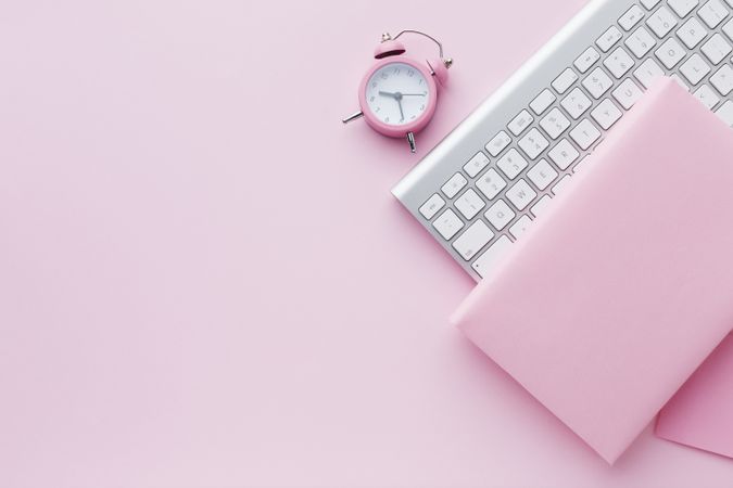 Top view of light pink book and clock with computer keyboard