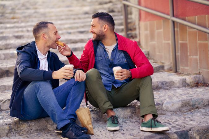 Two males sharing food while sitting outside with to go coffee