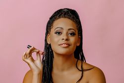 Confident Black woman holding lip gloss while looking at camera