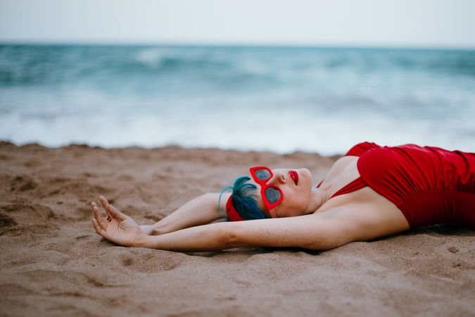 Relaxed woman in bright stylish swimsuit lying on sandy beach