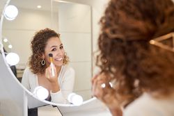 Smiling female applying powder on face with brush