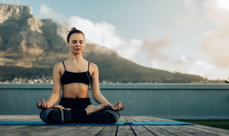Woman practicing yoga on the terrace of her home with mountains in the background