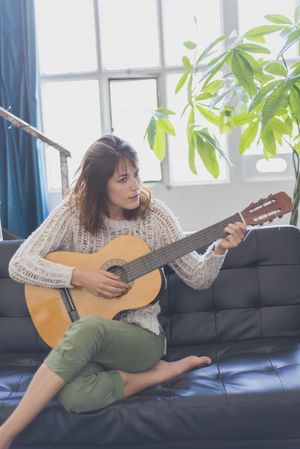 Female playing guitar in living room of bright loft