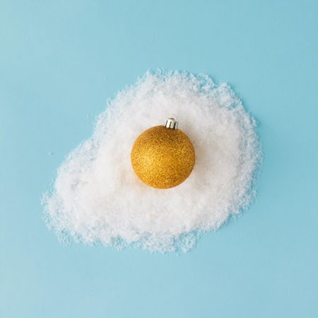 Egg made of golden Christmas bauble decoration and snow on blue background