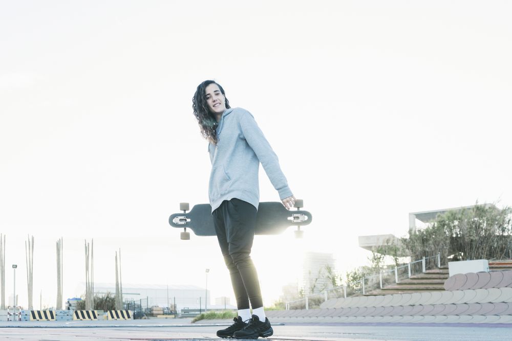 Low angle view of a teenage girl looking at camera while holding a longboard and smiling