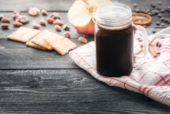 Jar with hot coffee and snacks on towel on rustic table