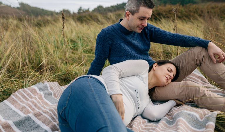 Man looking pregnant woman resting on the grass