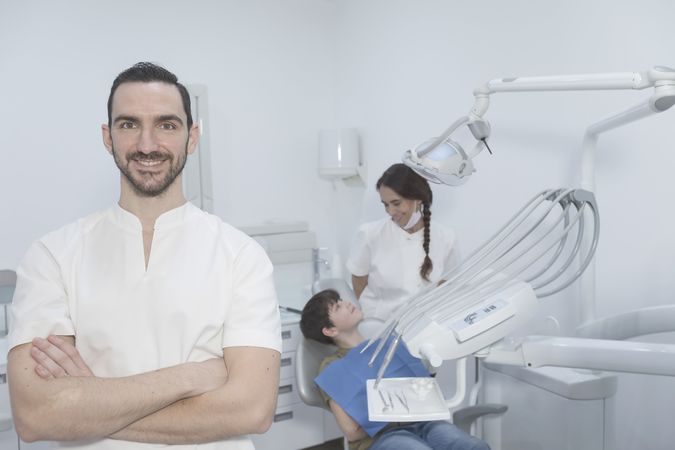 A portrait of a smiling dentist with teenage patient sitting in the background