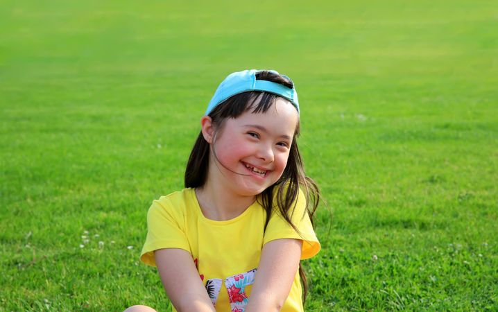 Girl with Down syndrome in a backwards cap sitting in the grass