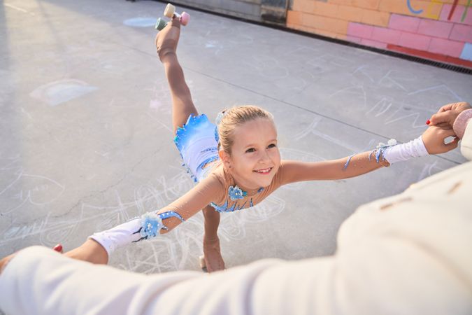 Cheerful girl in roller skates training with faceless trainer