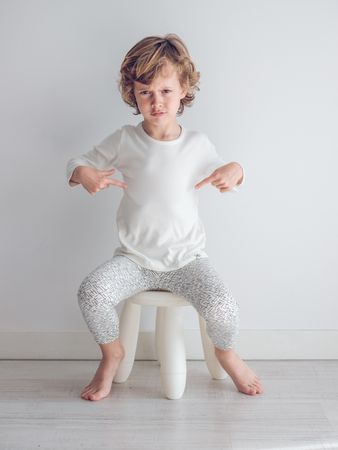 Boy in white pajamas leaning against the white wall of his house.