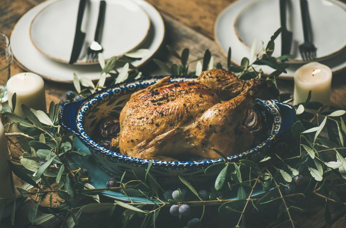 Centerpiece of roast chicken with two plates, decorative branches, candles