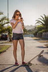 Young girl with a skateboard using the smartphone outdoor