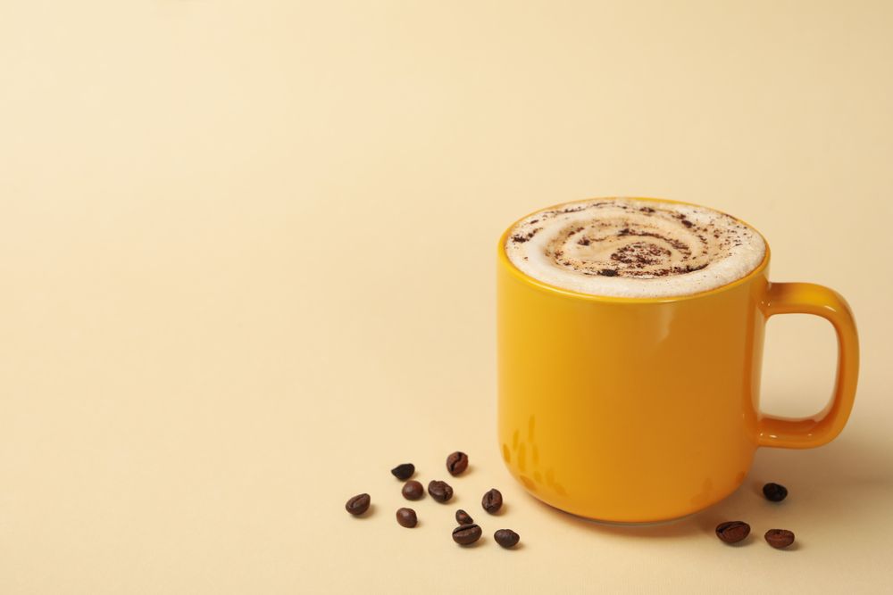 Cup of latte and coffee seeds on beige background
