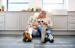Older couple kissing and toasting with red wine on kitchen floor 4ZDBr0