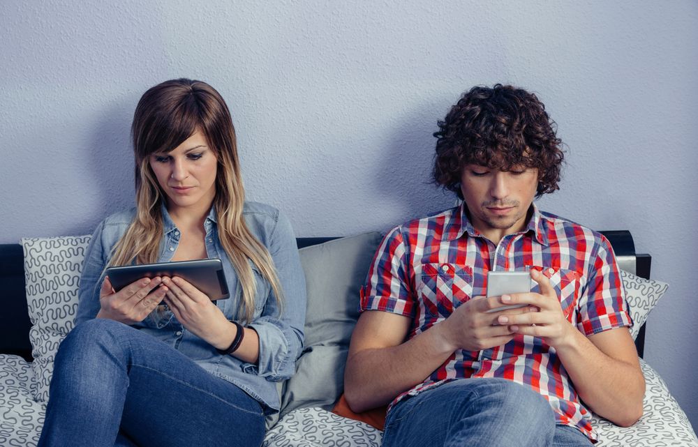 Couple in love using electronic devices relaxing on bed