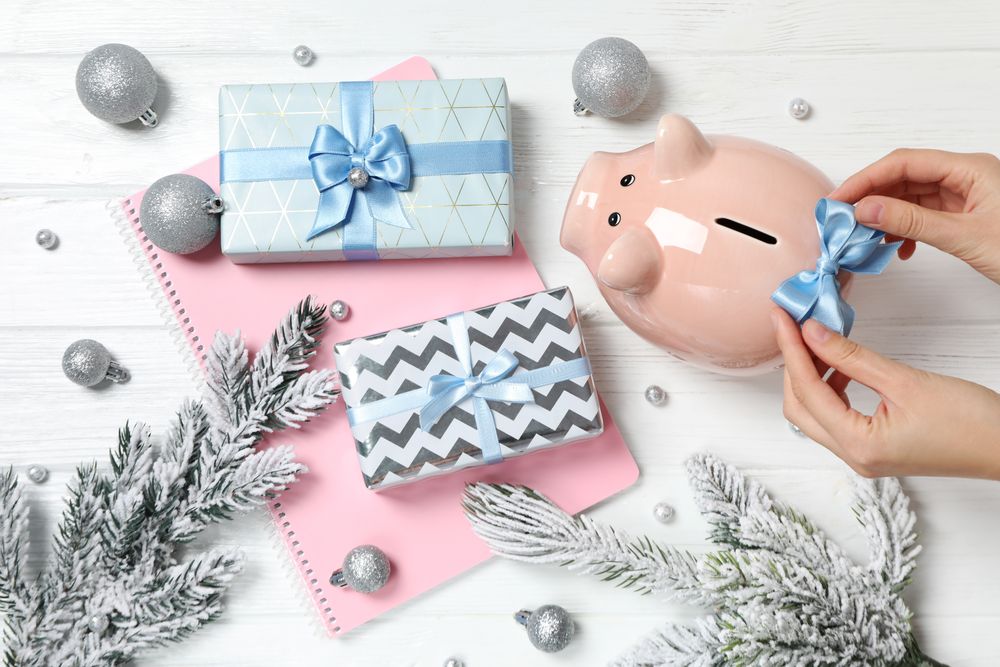 Piggy bank, notepad, gift boxes and hands on neutral wooden background, top view