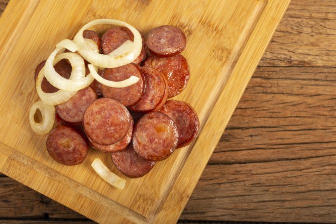 Sliced calabrese sausage with onion on wooden background.