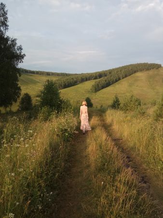 Back view of woman in pink dress walking on green grass field
