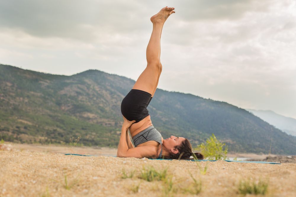 Woman practicing yoga outdoors near water
