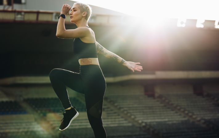 Woman doing high knee lifts in a stadium with sun in the background