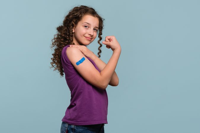 Girl flexing arm with blue bandage after receiving vaccine shot