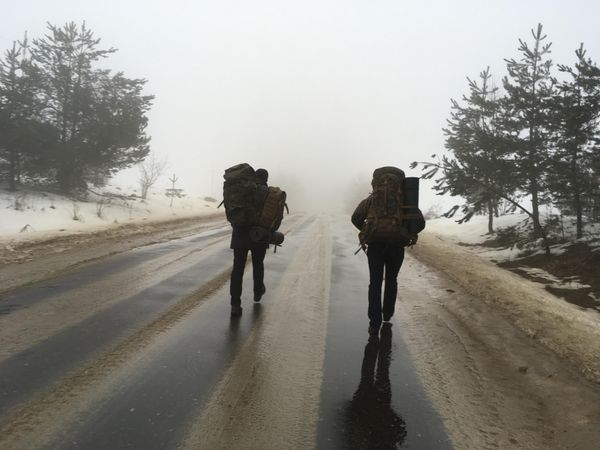 Two people with backpack walking on the road during winter