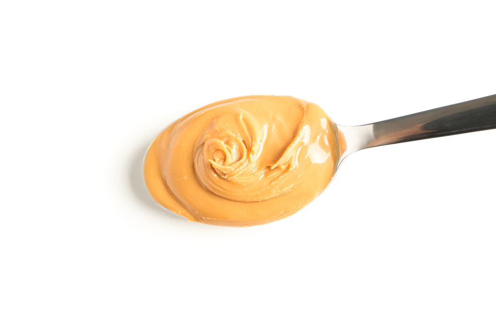 Creamy peanut butter in spoon isolated on light background, top view. A traditional product of American cuisine