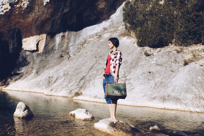 woman standing on rock with case near clear water in lake