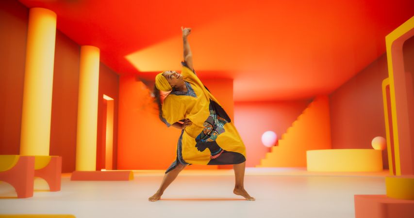 Black Woman in African Outfit Dancing Energetically in Geometric Abstract Orange Environment. Creative Female Performing Dance Choreography in a Studio, Making Moves, Having Fun, Practicing