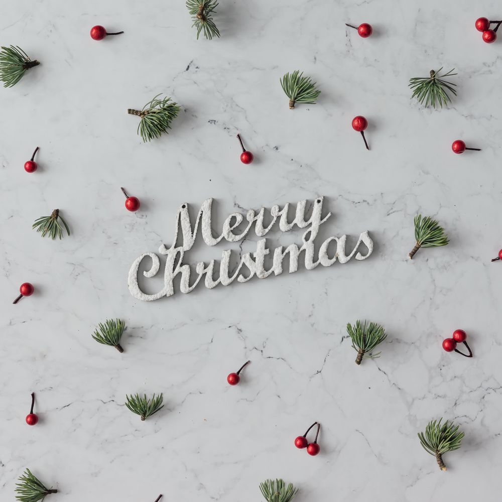 Holly and pine pattern on marble background with the words “Merry Christmas”