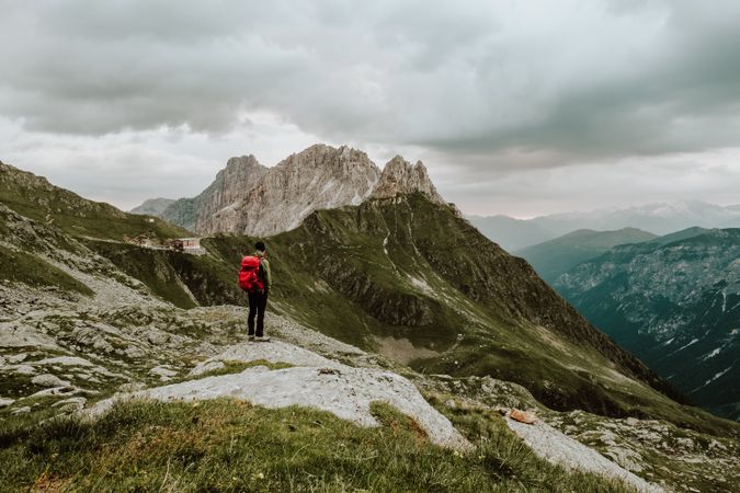 Person with backpack standing on rocky mountain under cloudy sky