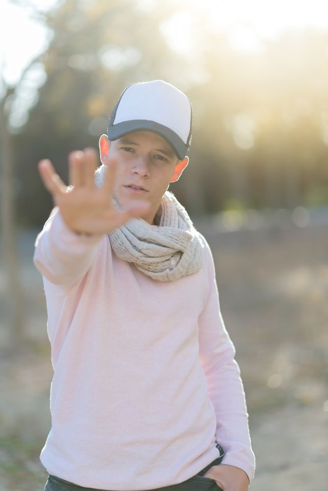 Teenage male wearing a cap with hand outreached saying "no"
