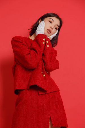 Woman in red skirt suit with light gloves touching her face