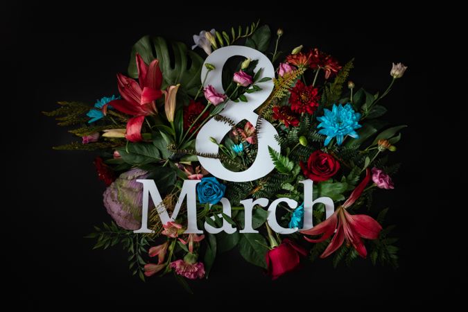 Colorful spring flowers of red, blue, pink, cream around “8 March” on dark background