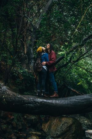 Young man hugging woman while standing on a log in the rain
