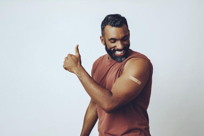 Proud man flexing arm with vaccination and giving thumbs up, copy space